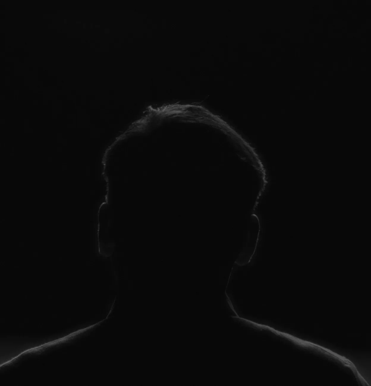 A person seen from behind in a dark room, the edges of their hair and shoulders caught by a soft light.